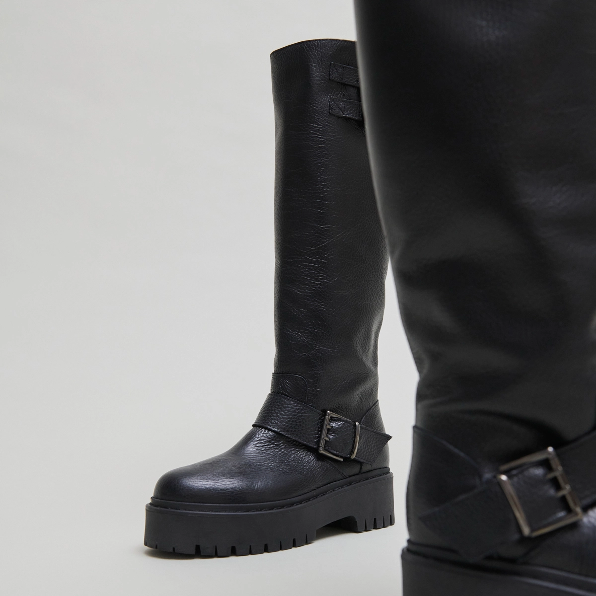 Boots with straps and notched soles in black grained leather | REINE