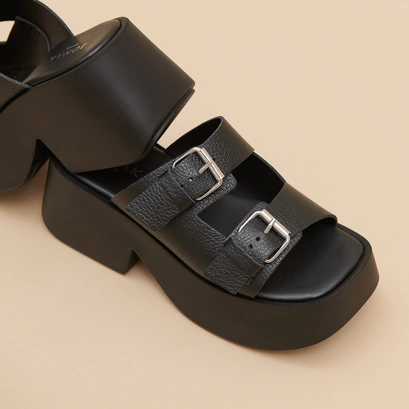 Mules with thick straps, buckles and open toes in black grained leather | ENOLA